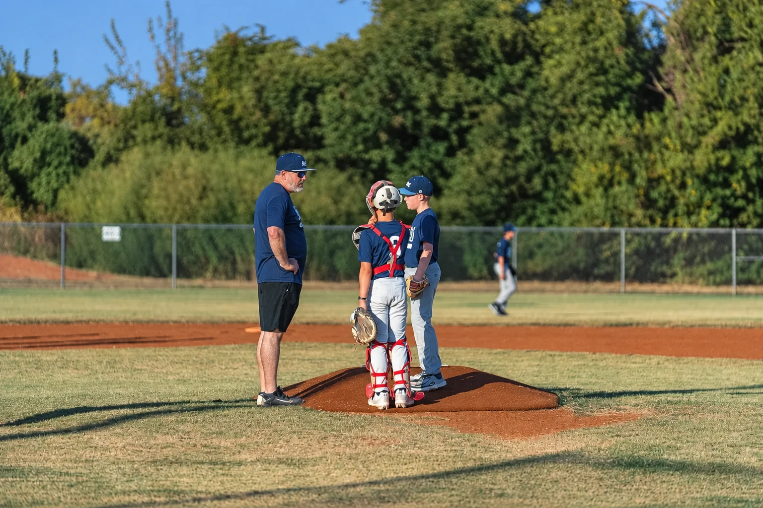 An SDG Baseball coach talking with two players on the mound